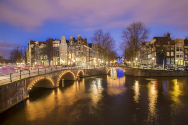 Amsterdam 'daki romantik kanal Leidsegracht' a gece şehir ışıkları, köprüler ve su üzerindeki yansıma