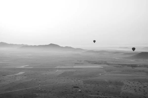 Fas 'ın yukarısındaki sıcak hava balonundan siyah beyaz bir resim. Havada iki balon daha var güzel bir dağ sırasının üstünde 