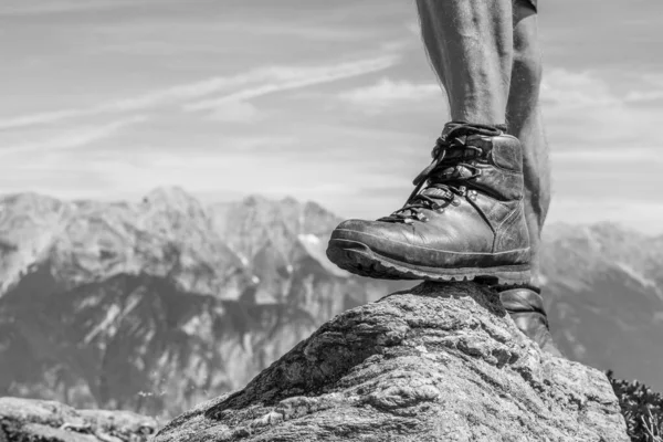 leather hiking shoe of a man stepping on a small rock in the Ziller Valley, Austria. Reaching the peak with a beautiful alpine mountain range in the background. Black and white
