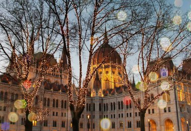 Noel 'de Budapeşte' de parlamento binası. Akşam yılbaşı ışıkları ve ağaçlardaki çelenkler, kış romantik manzarası