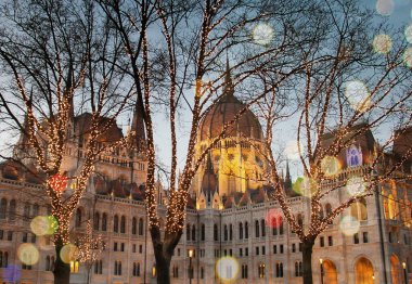 Noel 'de Budapeşte' de parlamento binası. Akşam yılbaşı ışıkları ve ağaçlardaki çelenkler, kış romantik manzarası