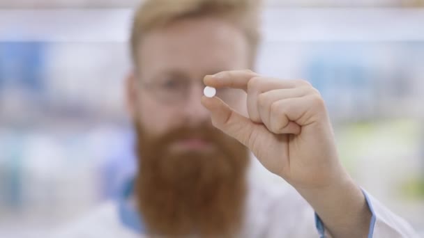 El joven doctor muestra una píldora redonda blanca y asiente con la cabeza aprobadamente — Vídeo de stock