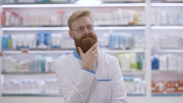 Joven médico o farmacéutico acariciando su barba y pensando — Vídeos de Stock