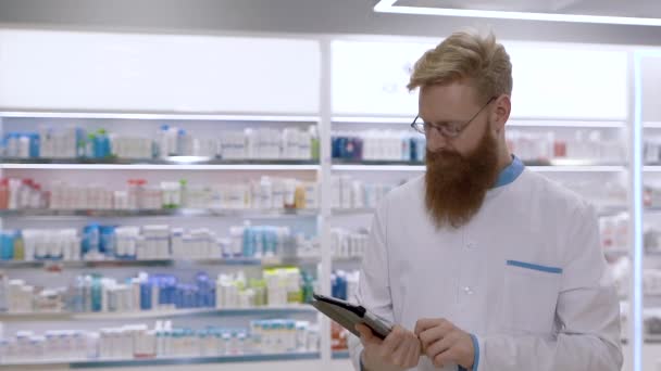 Un médico o farmacéutico joven usa una tableta y luego asiente con la cabeza desaprobadamente — Vídeo de stock