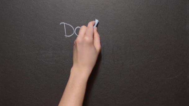 心配しないでください。左の女性の手は、黒い板の上にカラーチョークで「幸せになることを心配しないでください」という表現を書きます。女の子はすべての単語を書きます — ストック動画