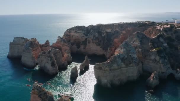 Vista aerea dal drone all'oceano Atlantico e barche in Portogallo. La gente naviga su una barca e fa surf. Rilassatevi in una bella giornata estiva sulla scogliera Ponta da Piedade nella città di Lagos — Video Stock
