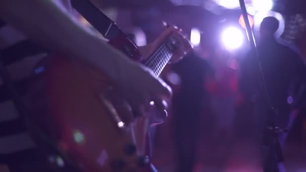 Kytarista hraje na kytaru s krumpáčem, dlouhé prsty na prkně pod tlumeným osvětlením, zblízka. Hudebník hrát moderní hudbu na profesionální nástroj v davu na nočním klubu party. — Stock video