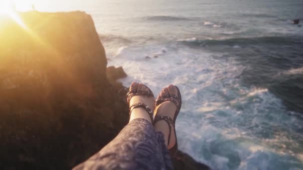 Bild av honfötter i sandaler på en klippa över havet. Vågor vackert bryta på klipporna i bakgrunden. Solnedgång — Stockvideo