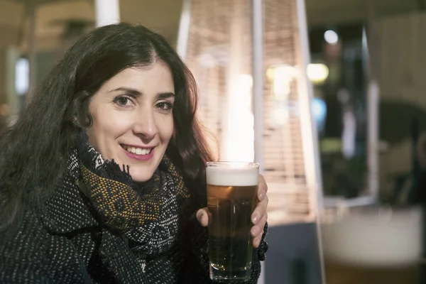 Cold icy woman drinks beer next to a gas stove, winter bar terrace image.