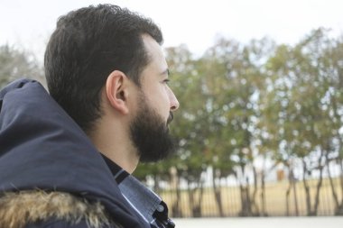 Sakallı adam profili. Açık hava parkına bakıyor.