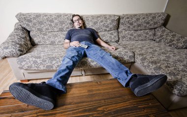 Adult man resting in sofa like a couch potato with remote control on belly clipart