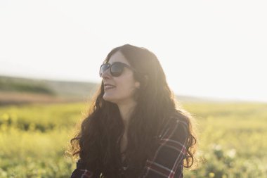 Bahar tarlasında güneş gözlüklü güzel kadın gülümsüyor.