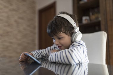 Evdeki çocuk dünyadan soyutlanmış kulaklıklarla telefona bakıyor.