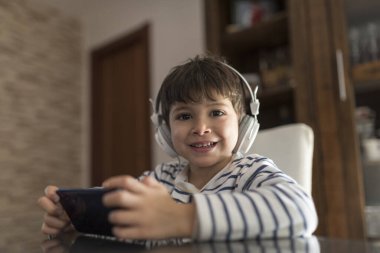 Evdeki çocuk dünyadan soyutlanmış kulaklıklarla telefona bakıyor.