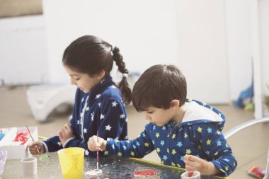 Evlerinin avlusunda iki kardeş seramik figürleri boyar ve konsantrasyonla el sanatları yaparlar.