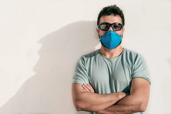 Man with facial mask and sunglasses looking at camera with crossed arms