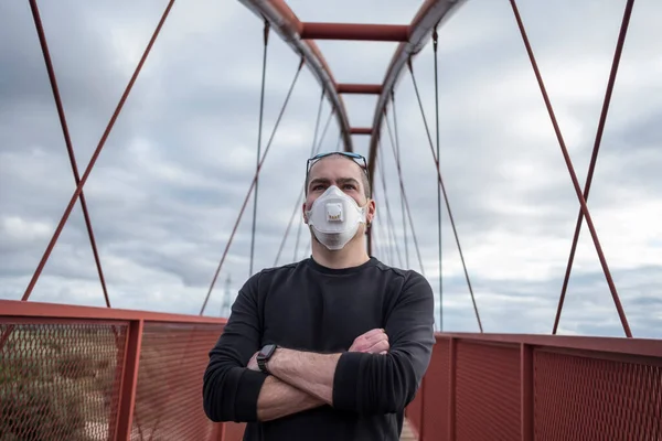 Man with surgery mask looking at camera in pedestrian bridge with crossed arms