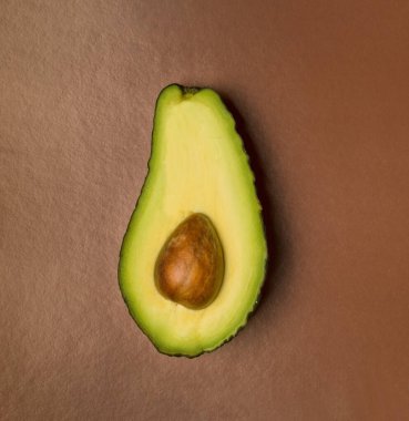 Kahverengi arka planda yarım avokado üst görünümü. Minimalizm.