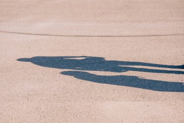 Sıcak bir yaz gününde asfaltta uzun gölgeli insan siluetleri. Yerde iki kişinin gölgesi..