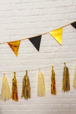 Beyaz bir duvarda altın renkli siyah çelenkler. İpte kağıt folyo bayrakları. Kağıt mendil püskülü çelenk Bunting mutlu yıllar düğün dekoru. Matte ve parlak altın çelenkler parti dekorasyonu için.