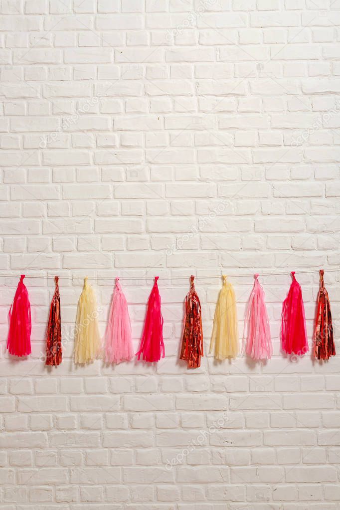 Pink yellow foil tissue paper garland on white brick wall. Paper fun decorations for birthday. Props for photo shoot booth decoration for holiday festival wedding party.