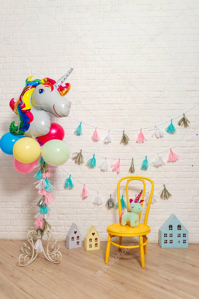 Balloons in the form of a unicorn. Idea for decorating unicorn style first year birthday party. Paper garlands on a white brick wall and photo booth props. Unicorn decoration for festival party for girl.