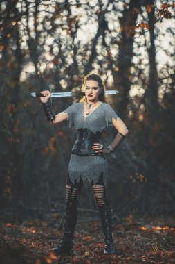 Metal kılıçlı gotik tarzda zırhlı kız şövalye. Kadın savaşçı Amazon Cadılar Bayramı için orman imajında.
