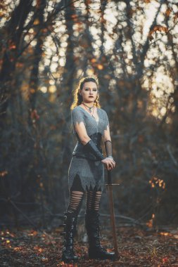 Metal kılıçlı gotik tarzda zırhlı kız şövalye. Kadın savaşçı Amazon Cadılar Bayramı için orman imajında.