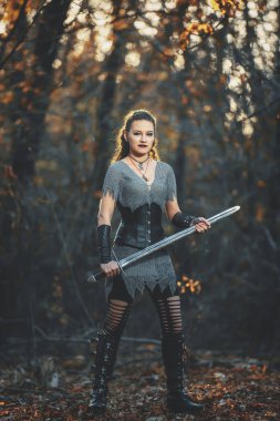 Metal kılıçlı gotik tarzda zırhlı kız şövalye. Kadın savaşçı Amazon Cadılar Bayramı için orman imajında.