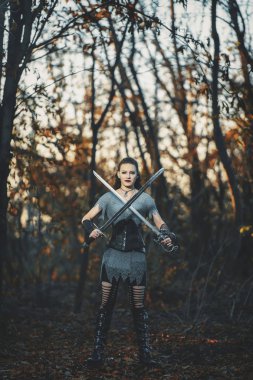 Metal kılıçlı gotik tarzda zırhlı kız şövalye. Kadın savaşçı Amazon Cadılar Bayramı için orman imajında.