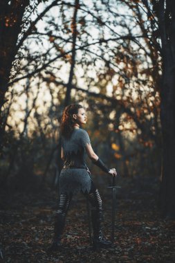 Metal kılıçlı gotik tarzda zırhlı kız şövalye. Kadın savaşçı Amazon Cadılar Bayramı için orman imajında.