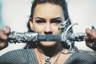 Gotik tarzda kılıç kostümlü zincirli bir kız şövalye. Cadılar Bayramı için savaşçı Amazon imajı. Kılıcı ejderha şeklinde kabzalı bir kadın..