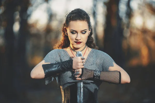 The girl knight in chain mail with a metal sword cosplay in Gothic style. Female warrior Amazon in the forest image for Halloween.