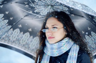 Şehirde kışın açık havada kar altında şemsiyeli kızlar. Gözlüklü romantik kız kışın kar altında sokakta vizyon peşinde. Güzel, genç, esmer kadın kış manzarasında