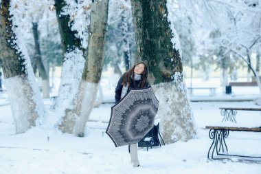 Şehirde kışın açık havada kar altında şemsiyeli kızlar. Gözlüklü romantik kız kışın kar altında sokakta vizyon peşinde. Güzel, genç, esmer kadın kış manzarasında