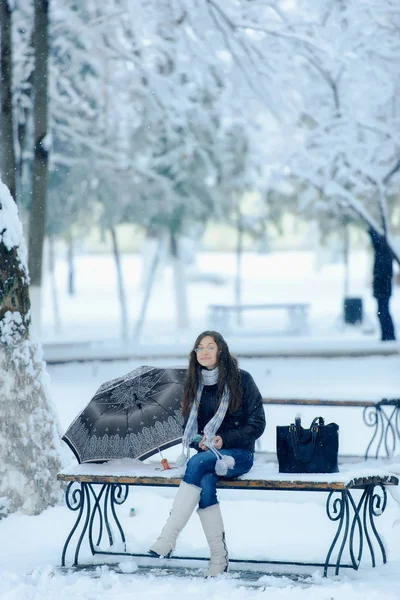 Girls with umbrella under snowfall in winter outdoor in the city. Romantic girl in glasses for vision on the street in winter under the snow. Beautiful young brunette woman in winter landscape