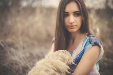 Kuru sazlıklar arasında güzel bir genç kadının portresi. Yazlık elbiseli esmer kız ilkbaharın başında. Güzel yüzlü kız, açık havada pampa otuyla paniğe kapılmış.