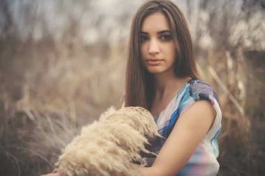 Kuru sazlıklar arasında güzel bir genç kadının portresi. Yazlık elbiseli esmer kız ilkbaharın başında. Güzel yüzlü kız, açık havada pampa otuyla paniğe kapılmış.