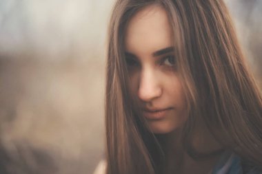 Baharın başında, arka planda ağaçların üzerinde uzun bir elbise giymiş güzel bir genç kadının portresi. Yazlık elbiseli esmer kız. Güzel yüzlü kız. Kapıları kapat.