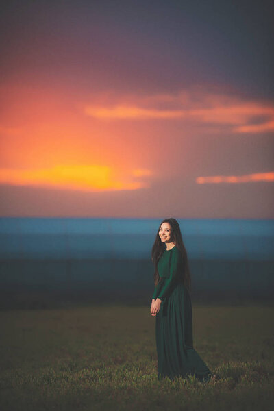 Красивая молодая женщина в длинном зеленом платье на фоне заката. Девушка в платье в поле на закате. Девушка на прогулке после заката
.