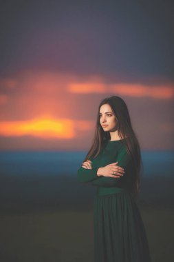 Gün batımı arka planında uzun yeşil elbiseli güzel genç bir kadının portresi. Gün batımında esmer bir kız. Gün batımından sonra güzel yüzlü bir kız.