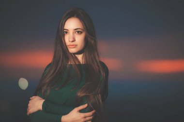 Gün batımı arka planında uzun yeşil elbiseli güzel genç bir kadının portresi. Gün batımında esmer bir kız. Gün batımından sonra güzel yüzlü bir kız.