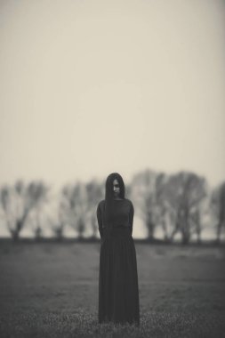 Girl in a long dress on the background of a gloomy forest black and white photo . A woman in a dark forest scary atmosphere like in a horror movie. An image of a girl from a Halloween horror movie.