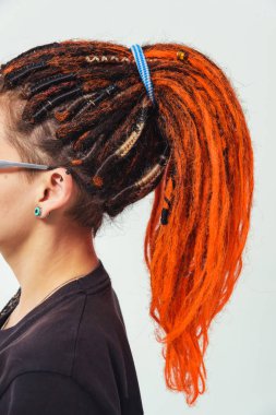 Ateşli kırmızı rastalı bir kız beyaz arka planda at kuyruğu ile bir araya geldi. Kafasında uzun kazayağı olan genç bir kadın. Turuncu saçlı ve piercingli kız.