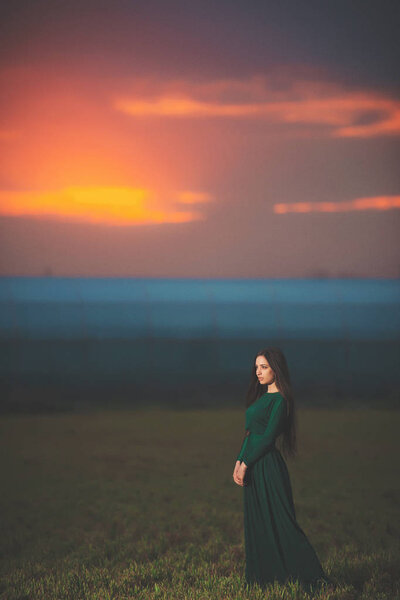 Красивая молодая женщина в длинном зеленом платье на фоне заката. Девушка в платье в поле на закате. Девушка на прогулке после заката
.