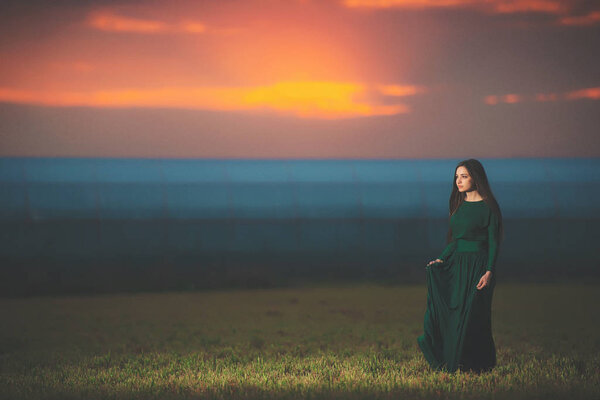 Красивая молодая женщина в длинном зеленом платье на фоне заката. Девушка в платье в поле на закате. Девушка на прогулке после заката
.