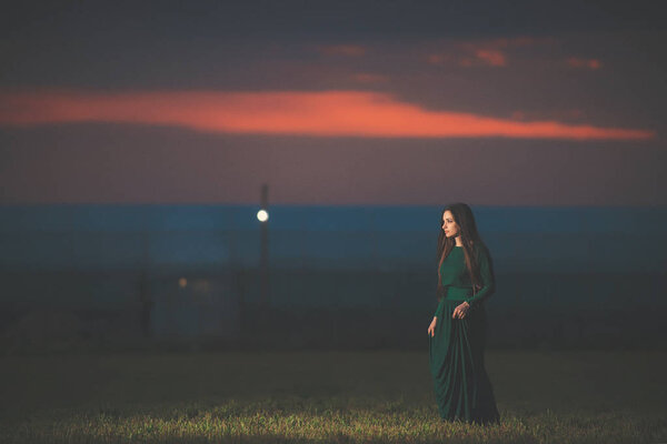 Красивая молодая женщина в длинном зеленом платье на фоне заката. Девушка в платье в поле на закате. Девушка на прогулке после заката
.