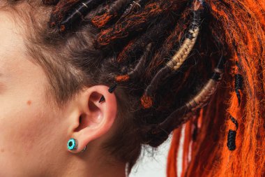 Ateşli kırmızı rastalı bir kız beyaz arka planda at kuyruğu ile bir araya geldi. Kafasında uzun kazayağı olan genç bir kadın. Turuncu saçlı ve piercingli kız.