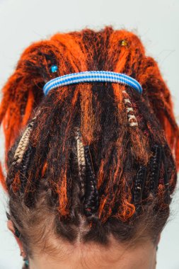 Kafasında süslemeler olan kızıl, doğal rastalı örgüler ve örgüler. Turuncu saçlar ve yakın plan mücevherler. At kuyruğu şeklinde toplanan saçlar için yapay rastalar. Saçlara örgü ve örgü örmek