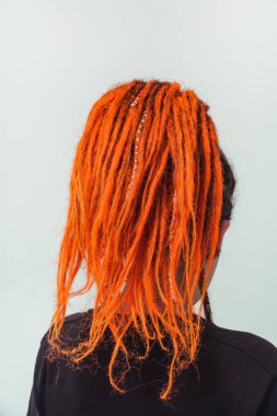 Kırmızı saçlı kız beyaz arka planda kuyruk şeklinde toplandı. Kafasında uzun kazayağı olan genç bir kadın. Turuncu rastalı ve piercingli gayri resmi kızlar.